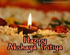 a lit candle sitting in the middle of flowers on top of a floor with words happy akshaya tritiya