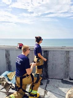 two fire fighters standing on top of a building next to the ocean