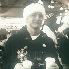 a man wearing a santa hat and holding two cups in his hands while standing next to other people