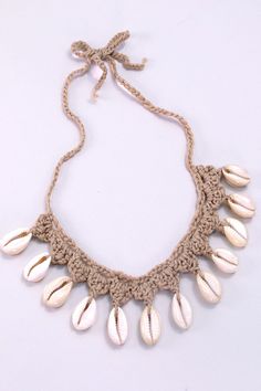 a crocheted necklace with shells hanging from it's side on a white surface