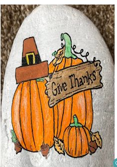 a painted rock with pumpkins and a sign that says give thanks to all of us