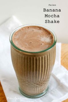 a glass filled with chocolate drink sitting on top of a white napkin next to a wooden table