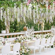 a long table with white chairs and flowers hanging from the ceiling