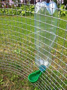 a green plastic cup sitting in the grass next to a wire fence with purple flowers behind it