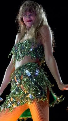 a woman in a green and orange outfit on stage with her legs spread wide open