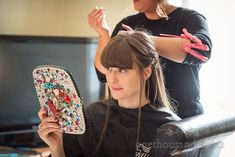 a woman is getting her hair done by another woman who is holding a comb and scissors