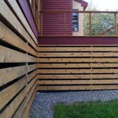 a wooden fence next to a house with red siding and green grass on the ground