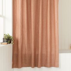 an orange curtain hanging in front of a window next to a potted plant on a shelf