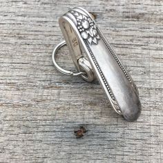 an old silver ring sitting on top of a wooden table next to a tiny piece of wood