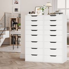 a white cabinet with black drawers in front of a stair case and stairs leading up to the second floor