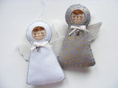 two small angel ornaments are sitting on a white tablecloth covered surface, one has an orange hair and the other is blue with gold stars