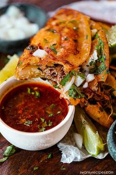 a large sandwich cut in half on top of a wooden table next to some dipping sauce