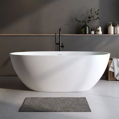 a large white bathtub sitting on top of a bathroom floor next to a rug