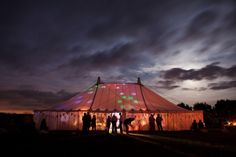 people standing in front of a large tent at night with lights on the side of it