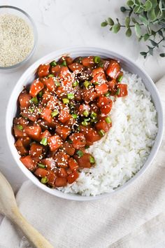 a white bowl filled with rice and meat on top of a table next to a wooden spoon