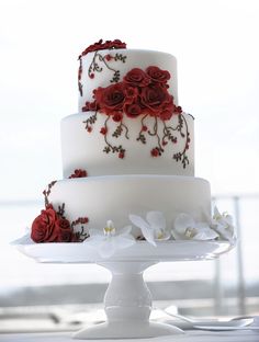 a three tiered white cake with red flowers on it