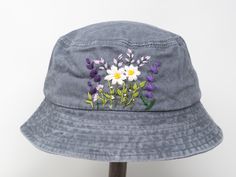 a gray hat with flowers embroidered on the front and side, sitting on top of a wooden stand