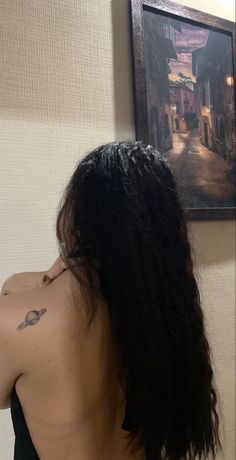 the back of a woman's head with long hair and tattoos on her left shoulder