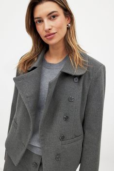 This jacket features a boxy fit and a rounded collar. It has shoulder pads and front pockets. The jacket has an asymmetric overlap design with a button closure and a lining.