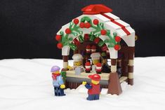 a small building made out of legos on top of snow covered ground with people standing around it