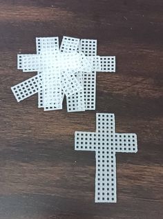 two pieces of white paper cut into the shape of a cross on a wooden surface