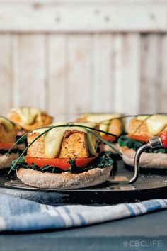 several sandwiches with cheese, tomatoes and spinach on a metal platter next to a blue towel