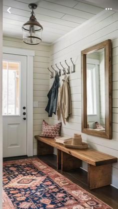 a hallway with a bench, mirror and coat rack on the wall next to a door