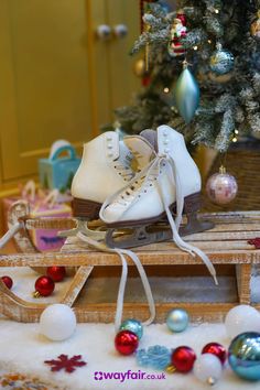 a pair of white ice skates sitting on top of a wooden sled next to a christmas tree