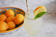 a glass filled with lemonade next to a bowl of oranges