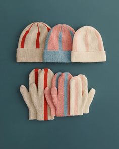 three knitted hats and mittens on a blue background, one with red stripes