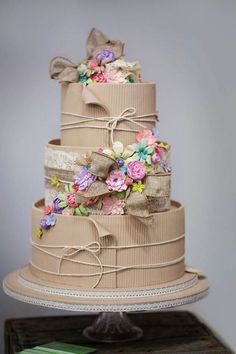 a three tiered cake decorated with flowers and burlap ribbons on top of a wooden table