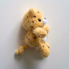 a yellow stuffed animal with black spots on it's face and arms, sitting up against a white wall