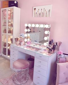 a pink room with a vanity, stool and mirror in the corner that has lights on it