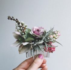 a hand holding a hair comb with flowers and greenery on the top of it