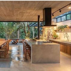 an open kitchen and dining room area with large wooden table in the center, surrounded by greenery