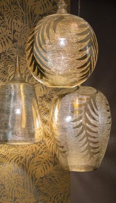 three glass lamps hanging from the ceiling in front of a wall with gold leaves on it