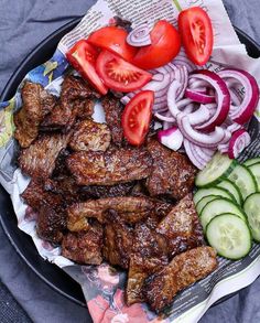 a plate full of meat, vegetables and sliced cucumbers on a table cloth