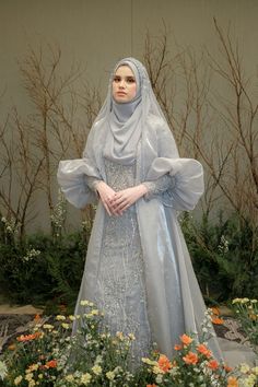 a woman in a dress and veil standing next to flowers