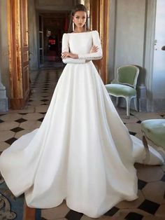 a woman in a white wedding dress standing next to a chair and door with her hands on her hips