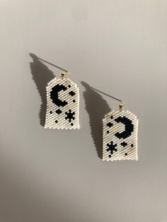 two small white and black beaded earrings with the letter c on it's side