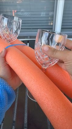 two people are holding up glasses and orange carrots on a grill with blue handles