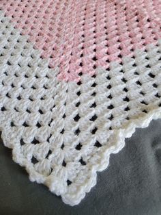 a pink and white crocheted blanket sitting on top of a gray bed sheet