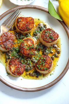 a white plate topped with scallops covered in sauce and garnished with parsley