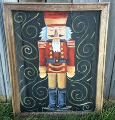 a painting of a nutcracker is displayed in front of a wooden frame on the grass