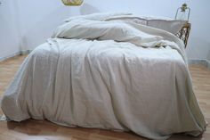 an unmade bed with white sheets and pillows on top of wooden floor next to lamp