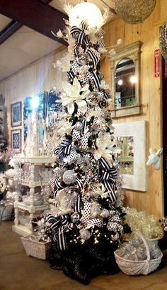 a white christmas tree with black and silver decorations in a room filled with other ornaments