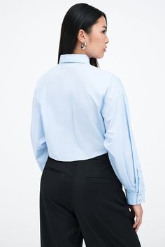 Our Ezra Shirt is a capsule wardrobe dream for your closet. Crafted from 100% crisp European poplin cotton, she offers a classic button-up silhouette in front, but with a cropped back for modern edge. Say hello, as well, to her diagonal seams at the front, sleek collar and long dolman sleeves finished with mother-of-pearl button cuffs. Wear Ezra tucked, tied or open and free—she never fails to inspire new looks.[SPLIT] Shannon, in light blue, is 5'8" (173 cm) tall, wearing a size M. Rocio, in li Cotton Cropped Shirt With Button Cuffs, Fitted Poplin Office Top, Fitted Poplin Top For Office, Classic Cropped Shirt With Button Cuffs, Classic Long Sleeve Cropped Shirt For Daywear, Fitted Poplin Tops For Work, Chic Cropped Shirt With Button Cuffs For Work, Chic Relaxed Fit Cropped Shirt For Workwear, Classic Button-up Cropped Shirt For Daywear