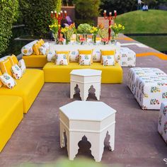 an outdoor seating area with yellow and white furniture, flowers and candles on the table