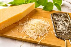 grated cheese on a wooden cutting board next to a grater and green leaves