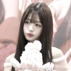 a woman with long black hair holding a white flower in her right hand and looking at the camera